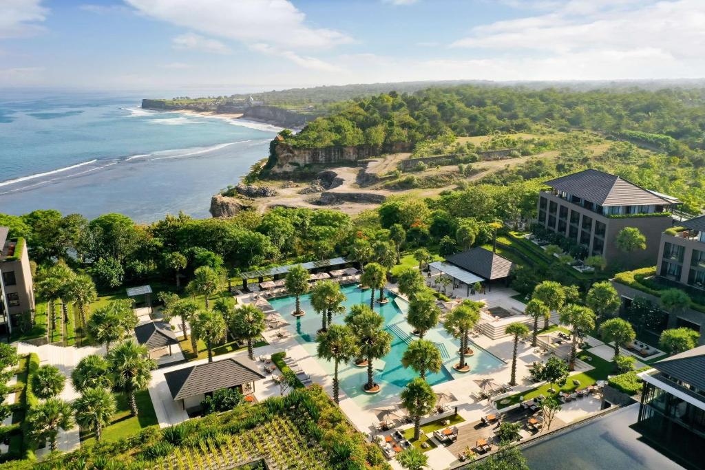 Vista aérea de um resort em Uluwatu com várias piscinas, rodeado de vegetação e falésias sobre o oceano, em Bali.