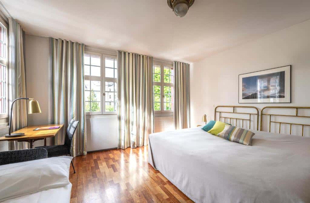 Quarto do Hotel Hofgarten Luzern, espaçoso, com cama de casal, sofá e secretária.