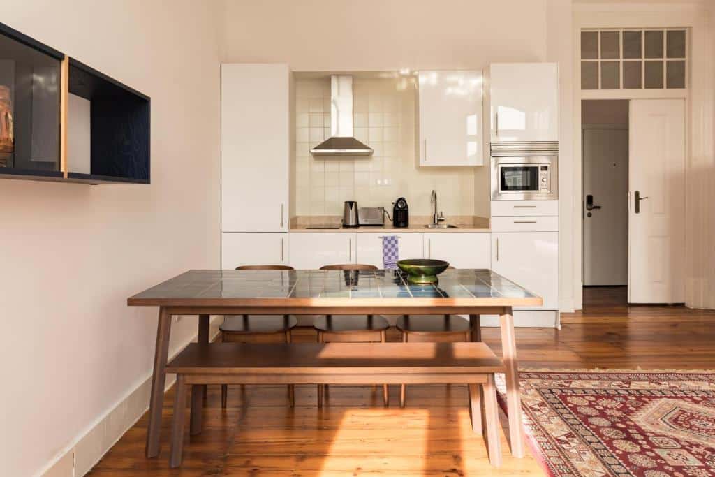 Cozinha compacta do The Visionaire Apartments com armários, placa, lava-loiça e alguns eletrodomésticos, além de uma mesa de madeira com seis lugares