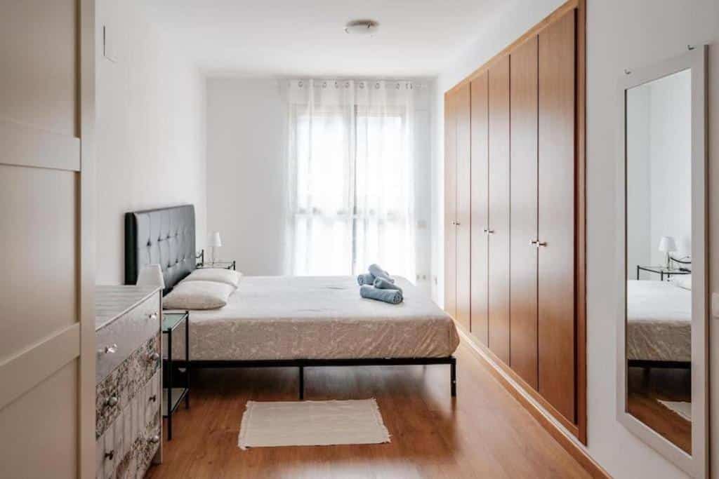 Quarto acolhedor do FiveStepsToSea, com cama de casal, roupeiro de madeira e espelho na parede.