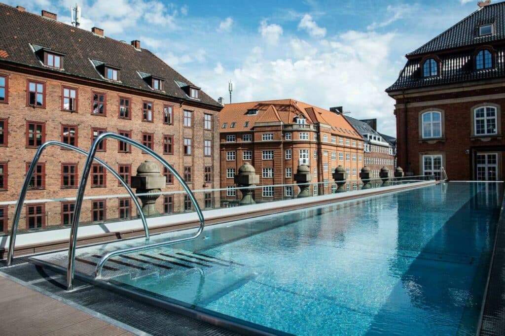 Piscina no terraço do hotel Villa Copenhagen, rodeada por vários edifícios.