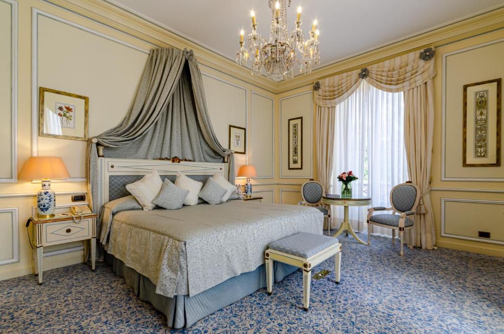 Quarto do Olissippo Lapa Palace com cama de casal, lustre, janela com cortinas e mesa com cadeiras estofadas, em estilo de época