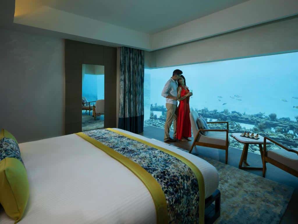Quarto de hotel com vista para aquário, casal a brindar num resort romântico paradisíaco das Maldivas