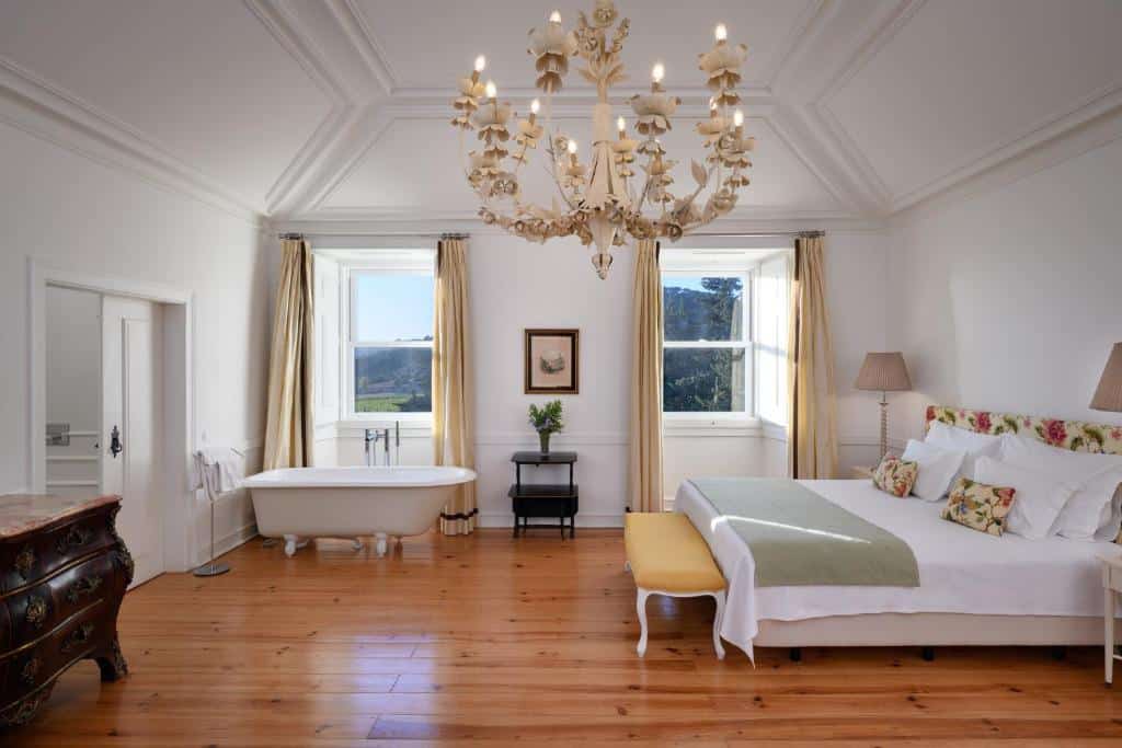 Quarto grande do Hotel Casa Palmela com cama de casal, banheira de louça branca e janelas com vista para a serra