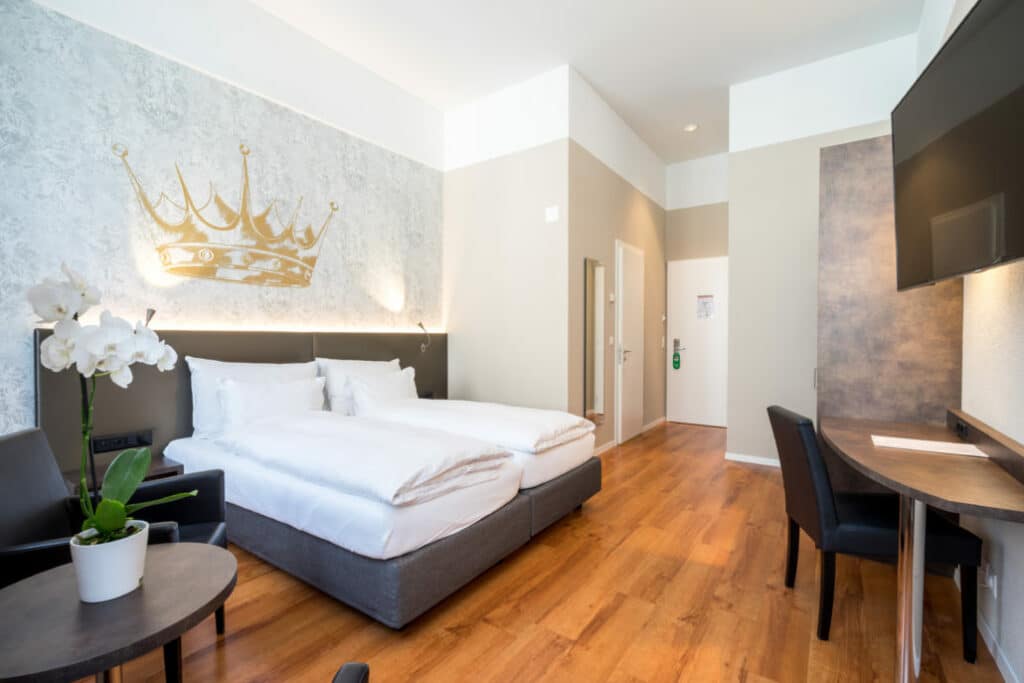 Quarto do Altstadt Hotel Krone Luzern, em Lucerna, com cama de casal e o logótipo da coroa na parede.