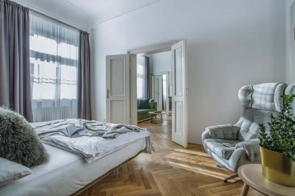 Quarto do Lazenska N4 Residence, com uma cama por fazer, uma poltrona, uma mesa lateral com uma planta e portas abertas para uma zona de estar.