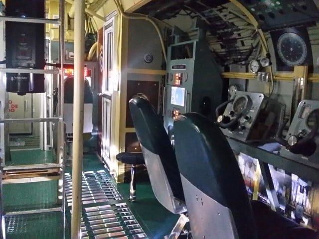 Interior apertado de um submarino em exposição no Museu Naval das Caraíbas, em Cartagena, com painéis de controlo, mostradores e uma escada metálica.