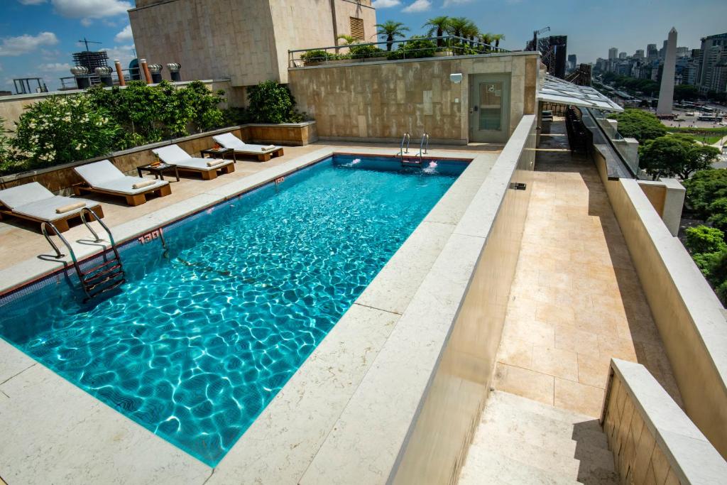 piscina retangular do Hotel Grand Brizo Buenos Aires, ao ar livre e com vista para a cidade, rodeada de espreguiçadeiras de madeira com almofadas brancas e plantas verdes