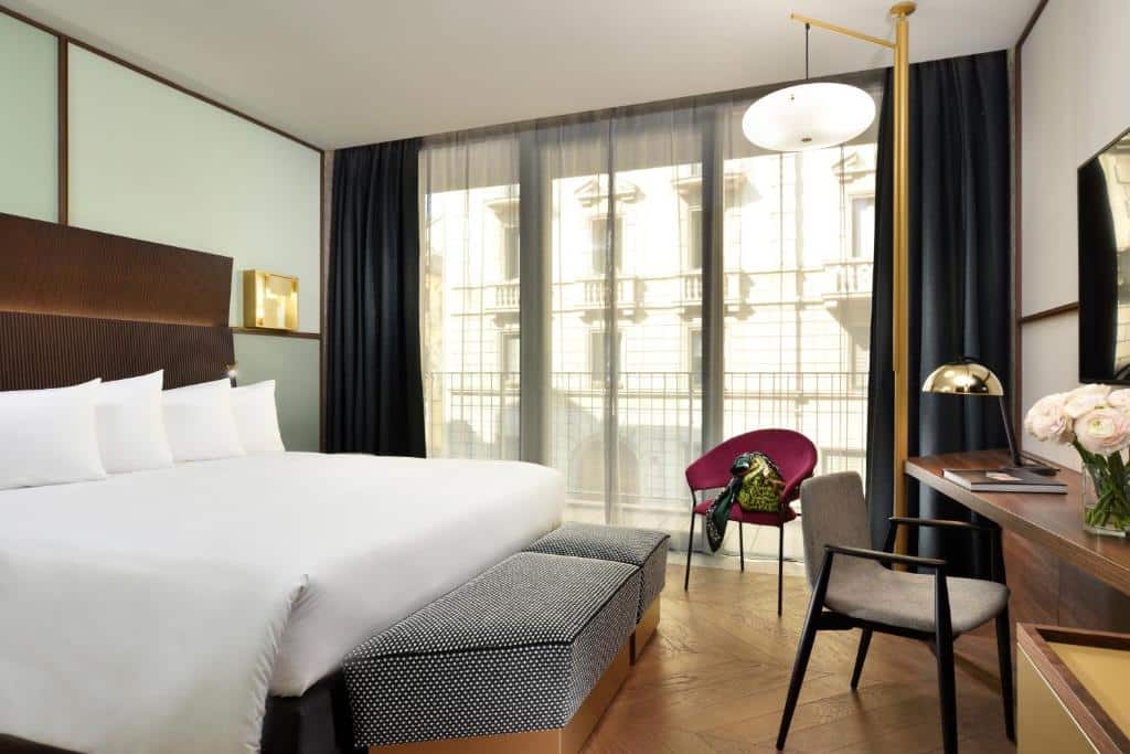 Quarto do Milano Verticale | UNA Esperienze com varanda ampla com cortinas, cama de casal com quatro almofadas, secretária e pavimento que imita madeira