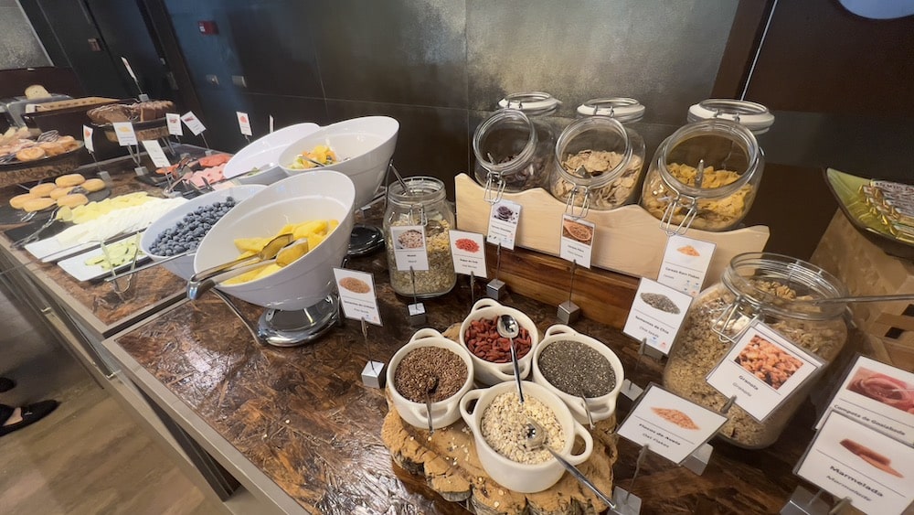 Buffet de pequeno-almoço com taças de fruta, frascos de granola e sementes e travessas de doces num balcão de madeira, no Neya Lisboa Hotel.