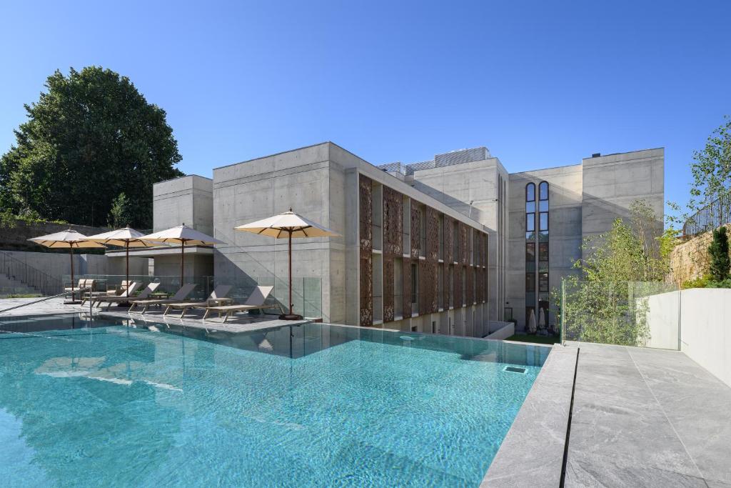 Edifício moderno em betão do INNSiDE by Meliá Braga Centro, com grandes janelas e piscina rodeada de espreguiçadeiras e chapéus de sol.