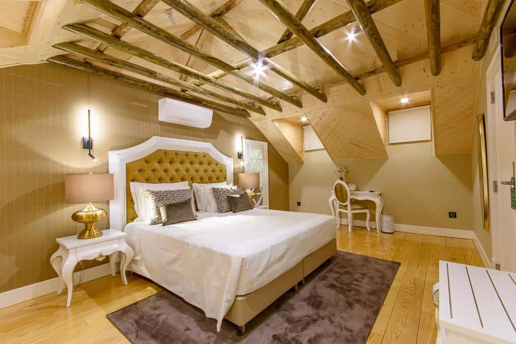 Um quarto com cama de casal, cabeceira dourada, vigas de madeira no teto, candeeiros e uma secretária com cadeira, na Villa Mariazinha Charming Hotel em Portimão.