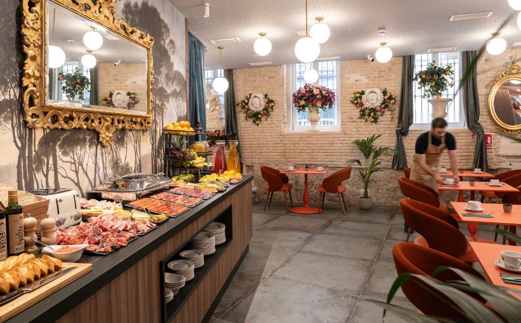 Salão decorado do Axel Hotel Valencia, com móveis retro, espelho dourado trabalhado, arranjos florais e pratos com vários alimentos num bufete rústico.