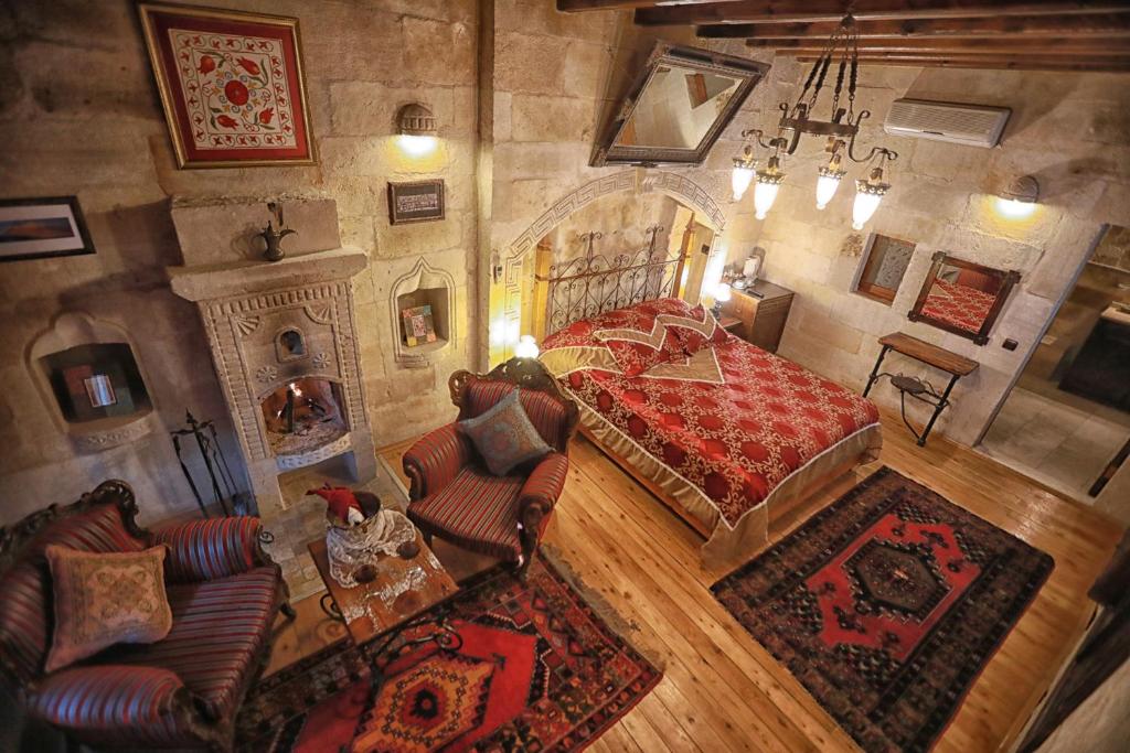 Quarto do Traveller's Cave Hotel, um dos hotéis da Capadócia, com paredes de pedra e iluminação acolhedora, cama de casal, lareira ornamentada, poltronas e tapetes estampados sobre soalho de madeira.