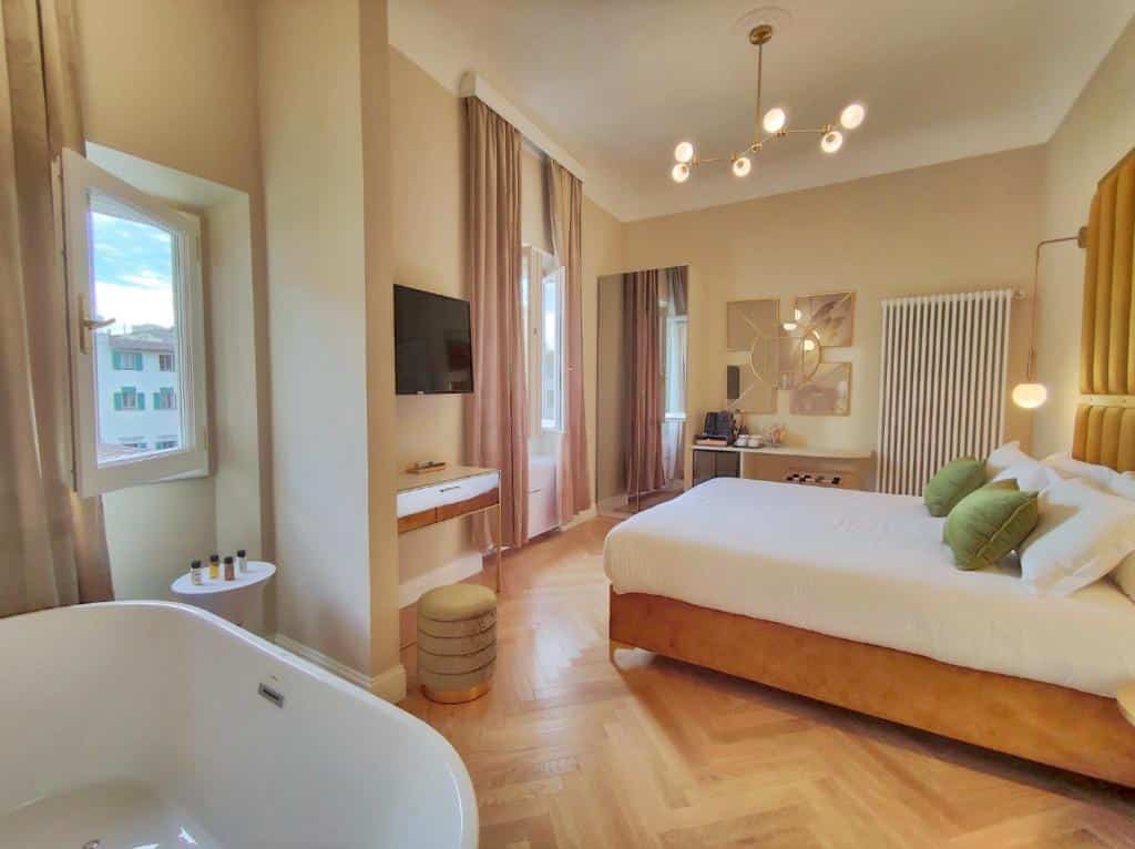 Quarto deluxe do Renascentia Garden Relais, de 28 m², com hidromassagem, cama de casal com almofadas, TV, espelho grande e mesa com utensílios para chá ou café