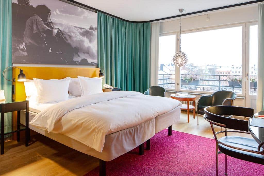 Quarto do Hotel Rival com cadeira, cama de casal e mesa redonda com cadeiras.