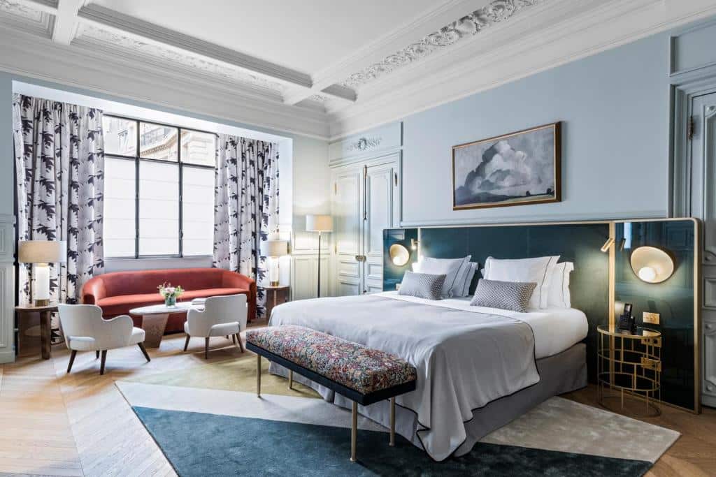Quarto elegante do Grand Powers Hotel com uma cama grande, área de estar, cortinas estampadas e obras de arte por cima da cabeceira da cama.