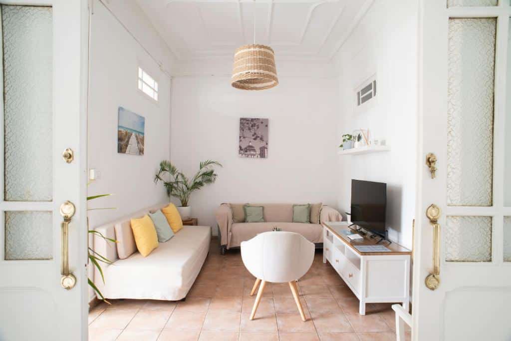 Sala de estar acolhedora do ABCyou Bed&amp;Breakfast, com sofá bege, almofadas decorativas, candeeiro de vime suspenso e móvel de TV branco com plantas na prateleira.