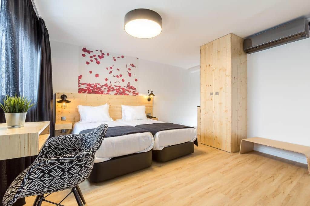 Quarto moderno no Hotel Santa Isabel com duas camas de solteiro, mobiliário de madeira, uma secretária com uma planta e uma arte na parede por cima das camas, para representar onde ficar em Fátima.