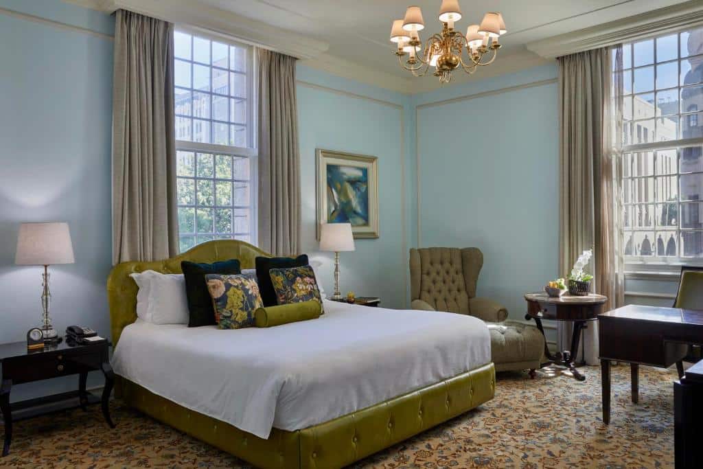 Quarto do Taj Cape Town com cama, duas janelas, poltrona, secretária, candeeiros e paredes azuis claras.
