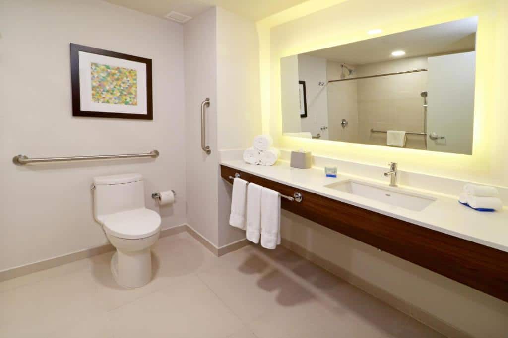 Casa de banho acessível do Holiday Inn Express & Suites com sanita, barras de apoio e lavatório com espaço livre para cadeira de rodas.