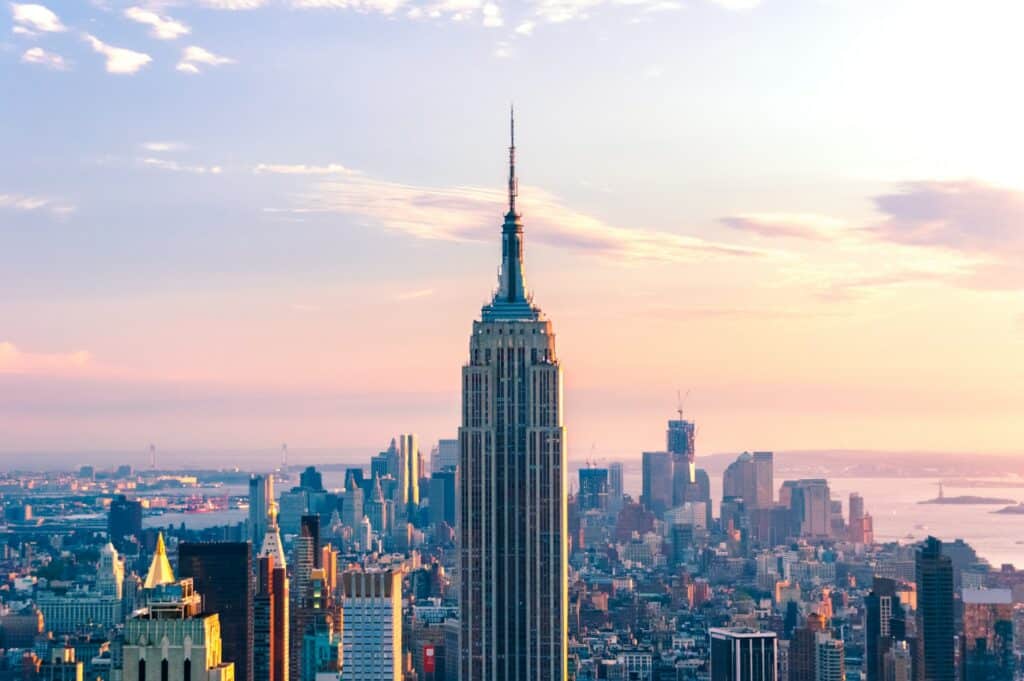 Vista do Empire State Building, uma das coisas a fazer em Nova York, com a sua torre imponente e pontiaguda rodeada de outros edifícios mais baixos ao final da tarde.
