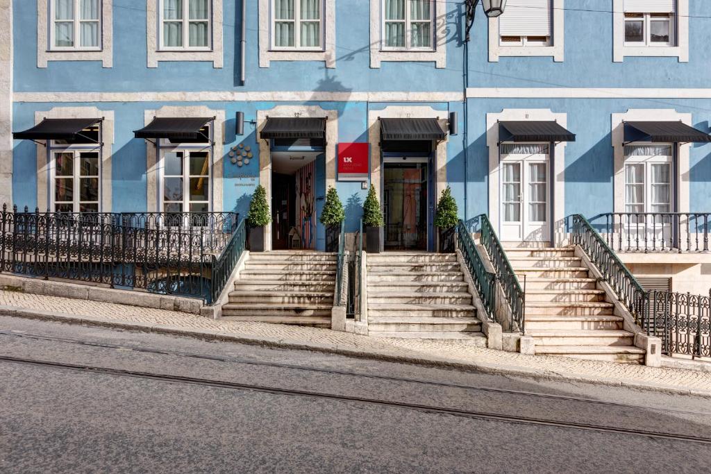 Três escadas com corrimão dão acesso às entradas de um edifício azul numa rua inclinada com carris de elétrico, no Lx Boutique Hotel.
