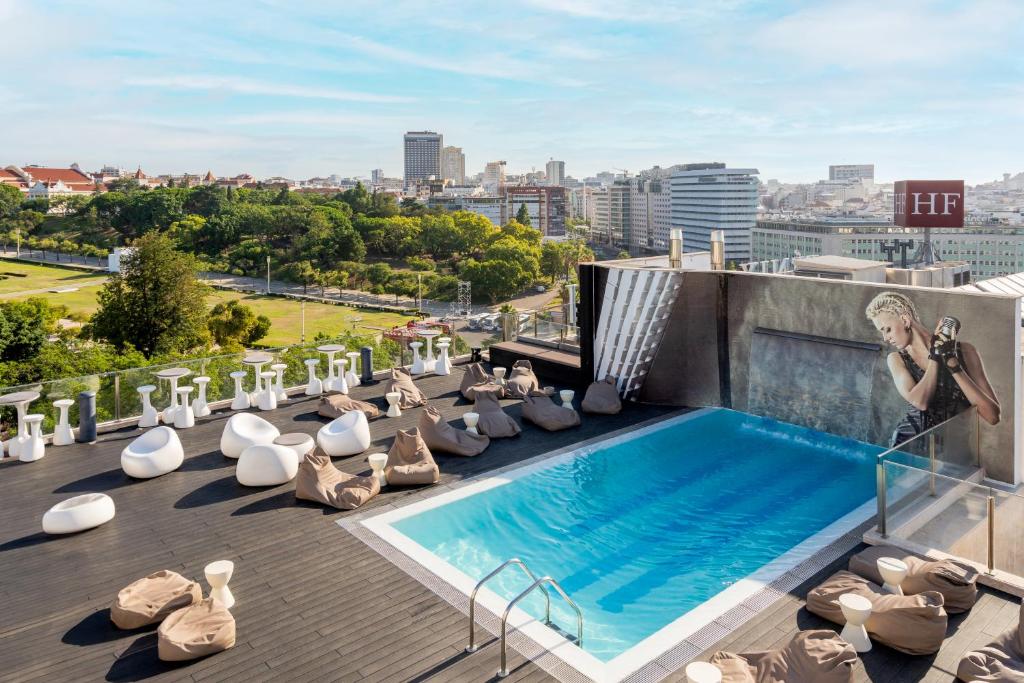 Piscina na cobertura do HF Fénix Music, com um deck espaçoso com mesas e bancos, pufes e uma bela vista sobre a cidade