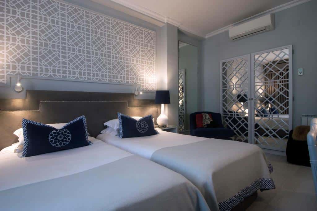 Um quarto no Coração de Fátima Boutique Hotel com duas camas de solteiro, almofadas estampadas, portas de armário espelhadas e decoração geométrica na parede atrás das camas, para representar onde ficar em Fátima.