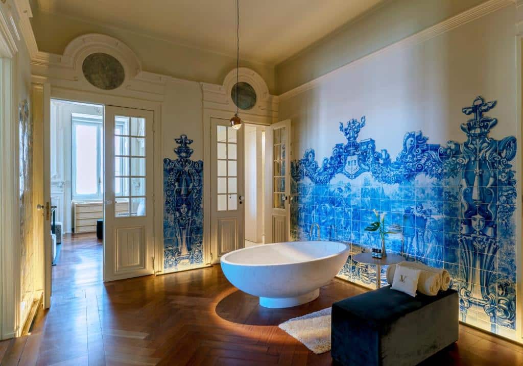 Casa de banho ampla do Verride Palácio Santa Catarina, com paredes revestidas a azulejos portugueses azuis e uma banheira oval ao centro, junto a um pequeno sofá com toalhas