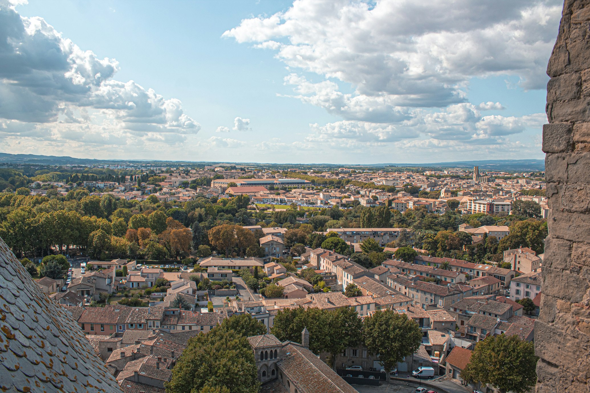 Vista aérea de Carcassonne, com edifícios agrupados, árvores e terras agrícolas vistas de uma estrutura de pedra.