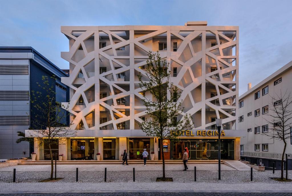Edifício de hotel moderno com fachada branca de linhas abstratas e a inscrição Hotel Regina, com pessoas a passar em frente.