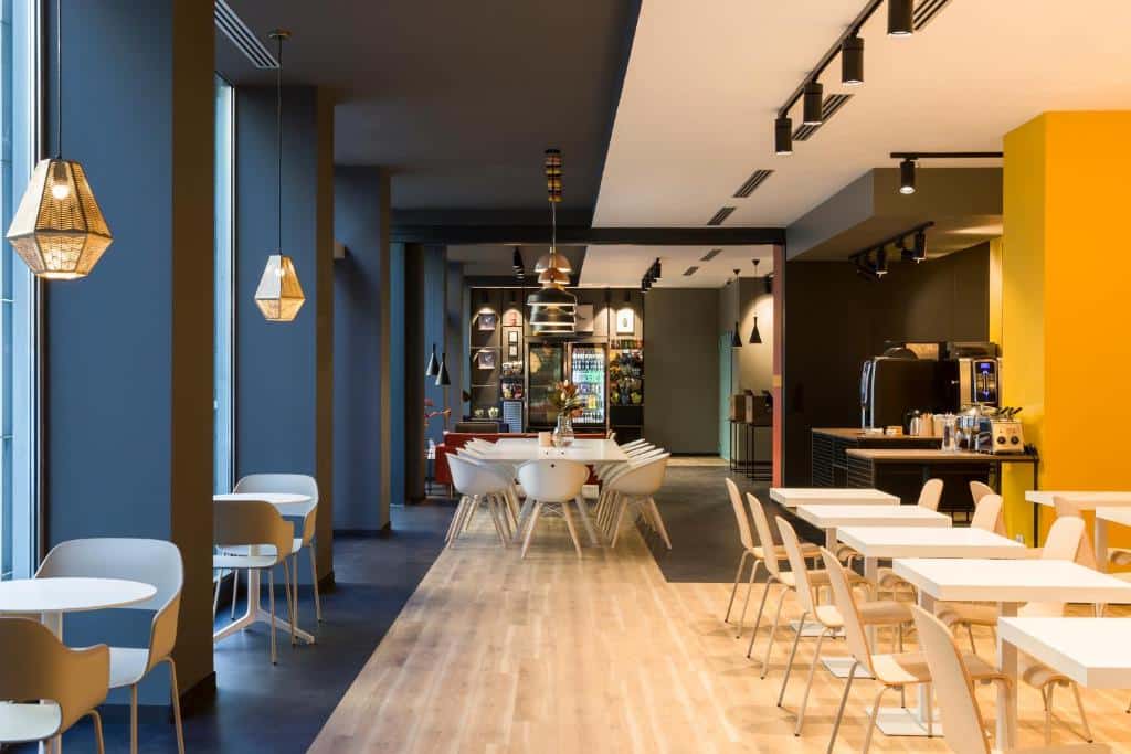 Zona de refeições do B&amp;B Hotel Milano Central Station com mesas quadradas e cadeiras, candeeiros pelo espaço e uma mesa com máquinas de café e chávenas