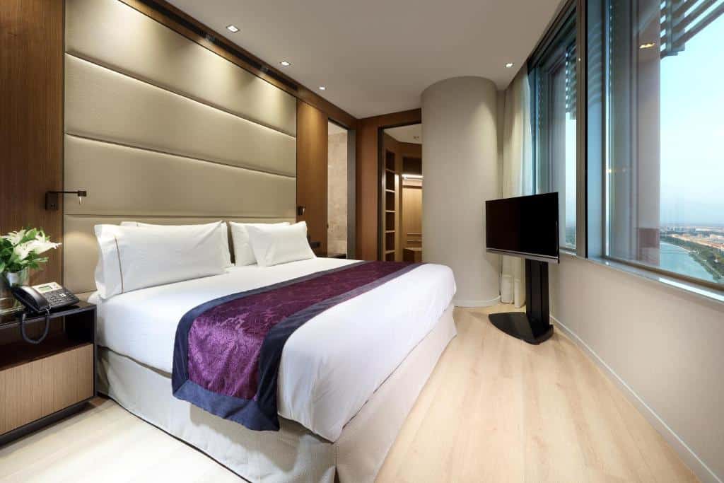 Quarto do Eurostars Torre Sevilla com cama de casal e uma janela ampla com vista para a cidade.