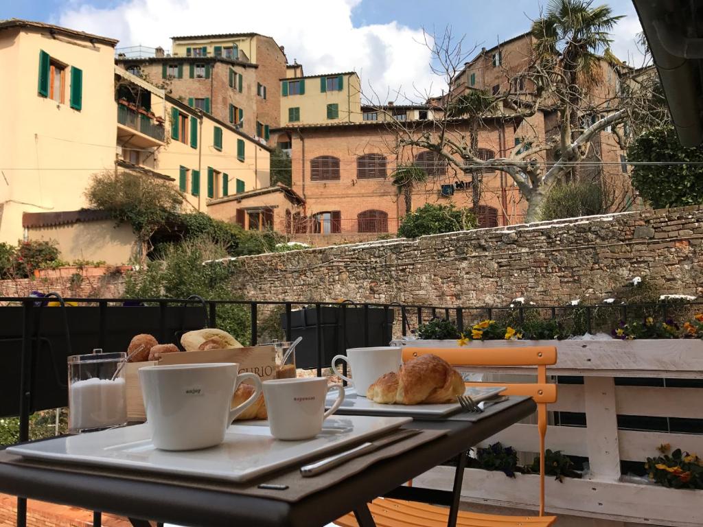 Mesa com chávenas e pães na varanda de um dos hotéis na Toscana, com vista sobre outros edifícios alaranjados da região e um muro de tijolo