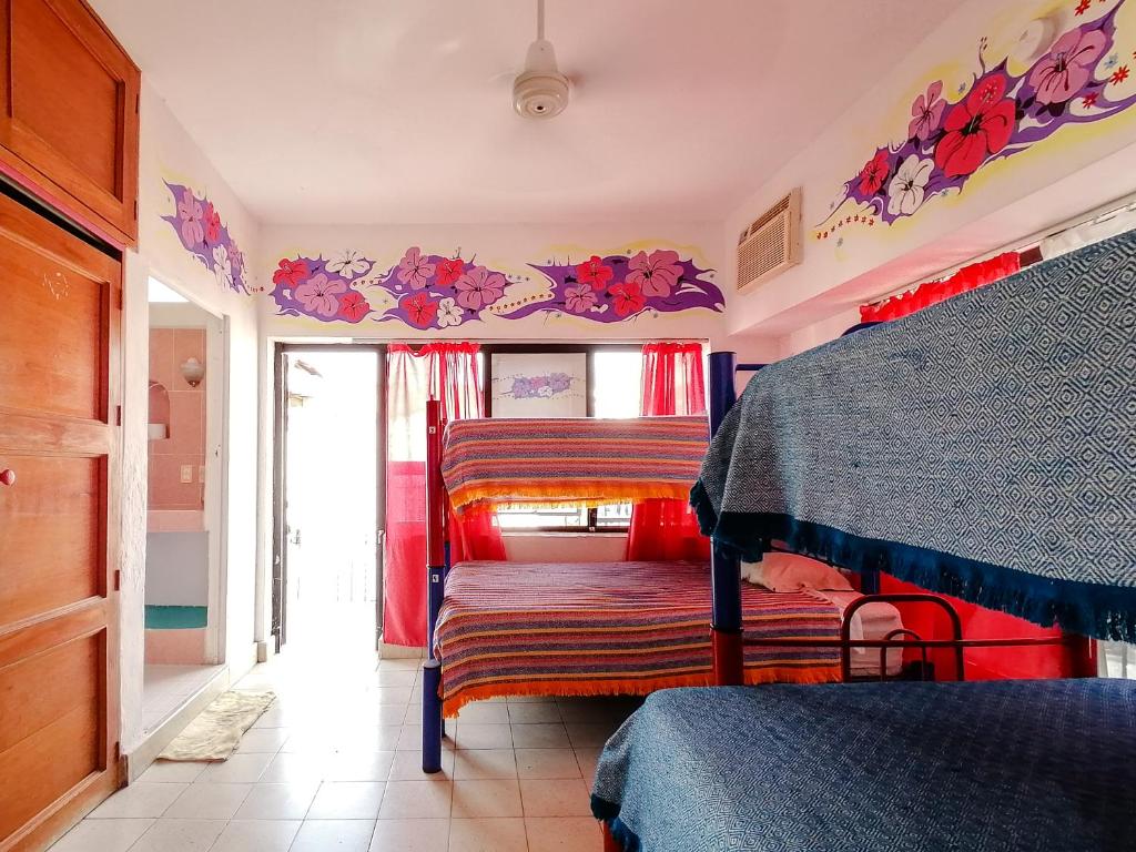 Um quarto bem iluminado com beliches, cobertores coloridos, arte floral na parede, pavimento de ladrilho e uma ventoinha de teto.