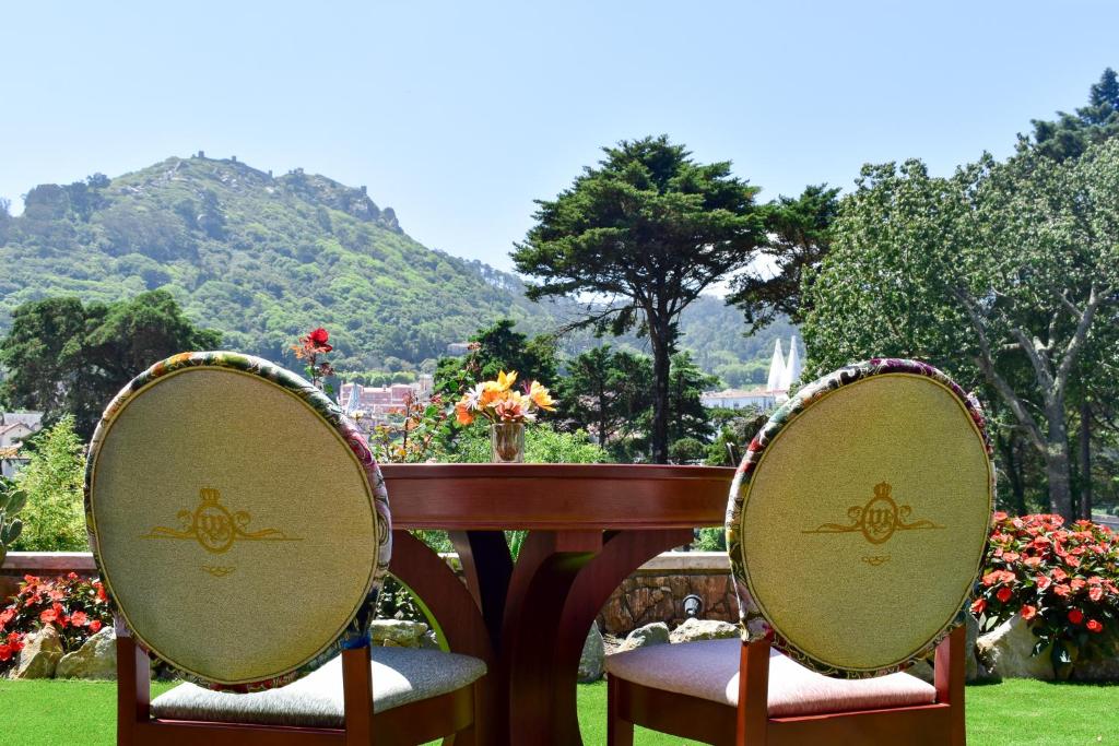 Jardim do Sintra Marmoris Palace com mesa redonda de madeira e duas cadeiras de frente para as flores e a serra