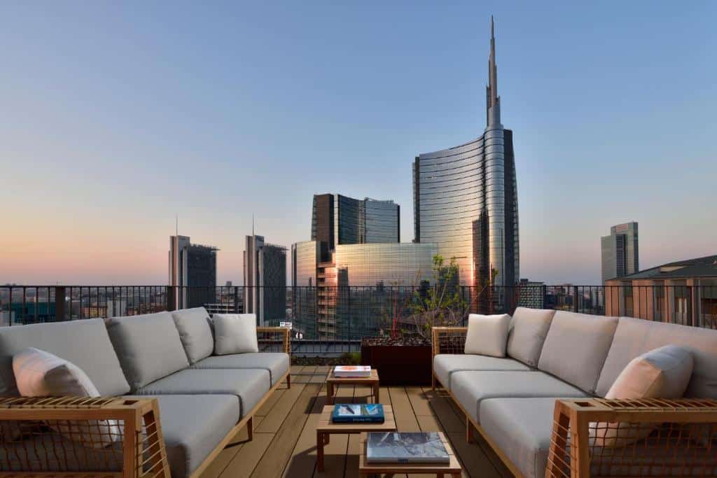 Terraço com dois sofás compridos frente a frente e vista sobre os edifícios ao entardecer no Milano Verticale | UNA Esperienze