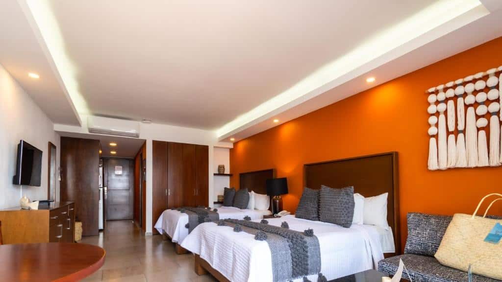 Quarto do The Paramar Beachfront Boutique Hotel com duas camas de casal, parede com detalhes em laranja, decoração moderna, TV, móveis de madeira e iluminação suave.