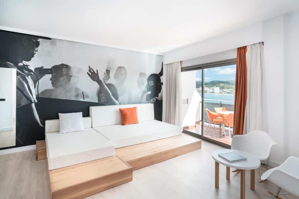 Quarto moderno do THB Ocean Beach com mobiliário branco, um mural a preto e branco e uma varanda com vista para a cidade e a montanha.