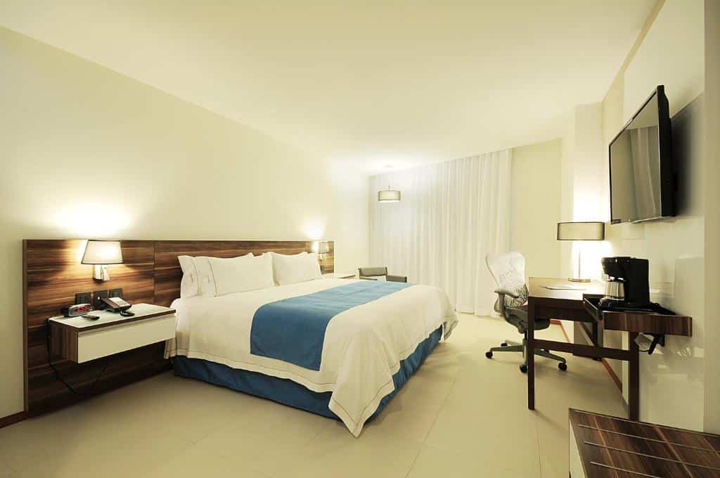 Quarto do Holiday Inn Express Puerto Vallarta com uma cama king-size, secretária, cadeira, TV, máquina de café e candeeiros de cabeceira, em tons neutros.