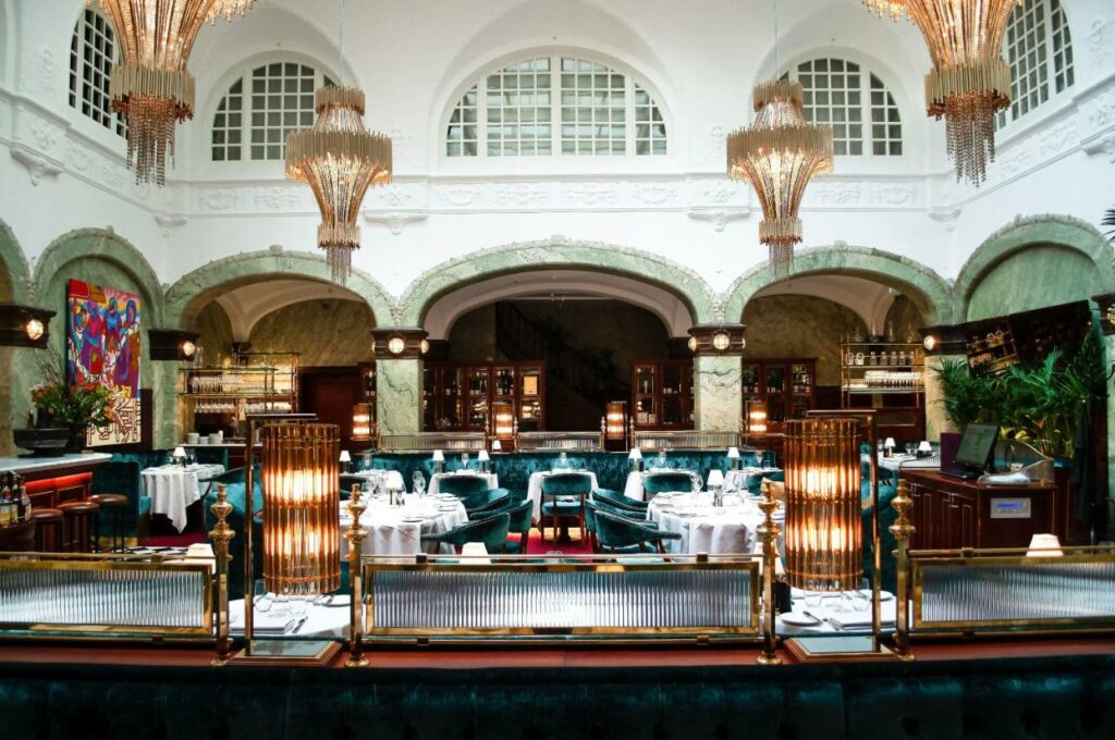Restaurante do Bank Hotel, em Estocolmo, com arquitetura histórica, lustres e mesas com cadeiras estofadas.