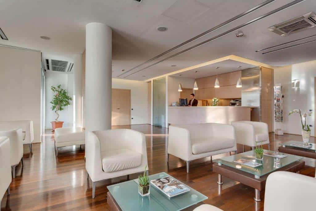 Receção de hotel moderno com poltronas brancas, mesa de centro e balcão de atendimento
