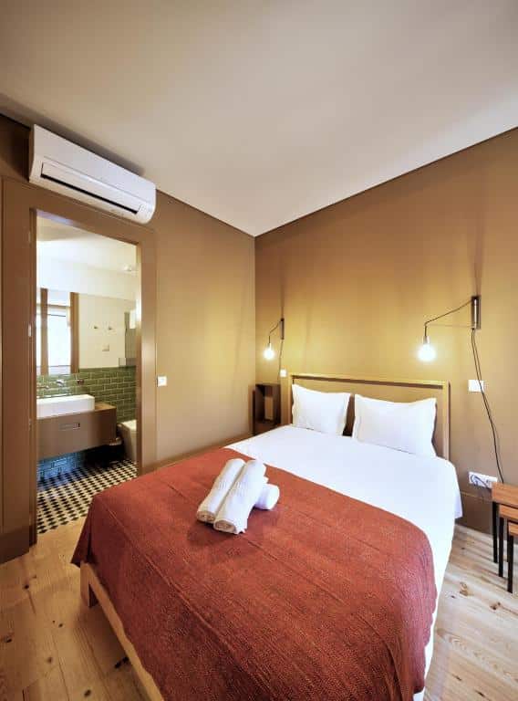 Quarto do Aparthotel Oporto Batalha, com cama de casal à direita e, à esquerda, a porta que dá acesso à casa de banho.