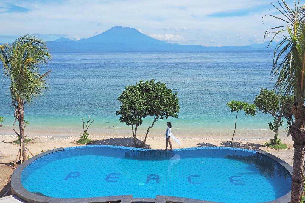 Pessoa de branco junto a uma piscina com vista para a praia e a montanha, num resort em Nusa Penida, Bali.
