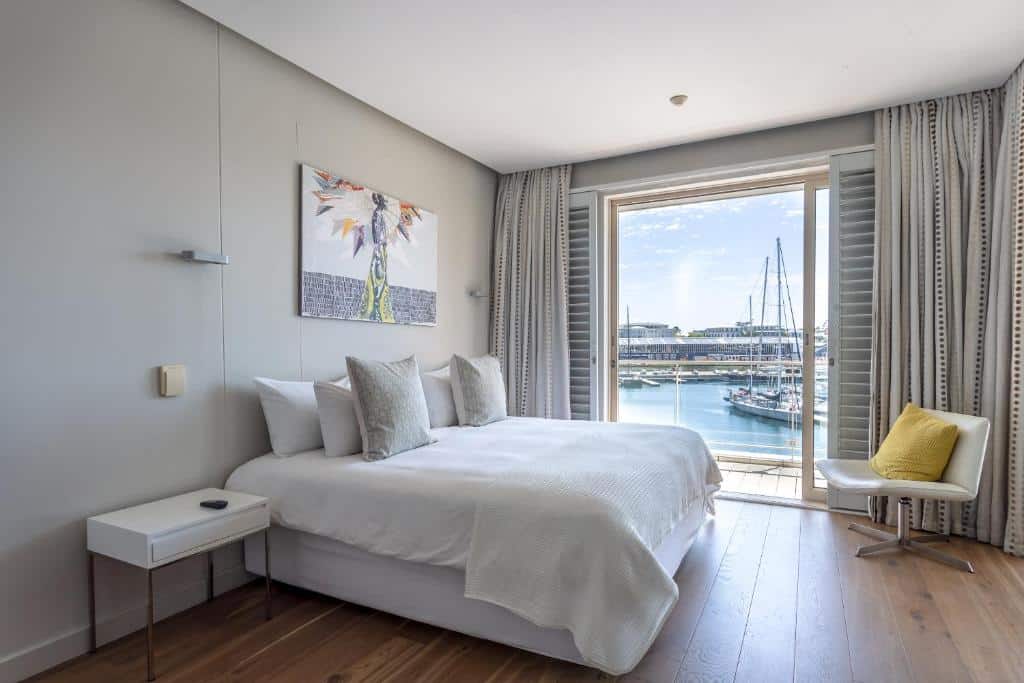 Quarto no Atlantic Marina com cama de casal, roupa de cama branca, mesa lateral, cadeira e janela com vista para a marina.