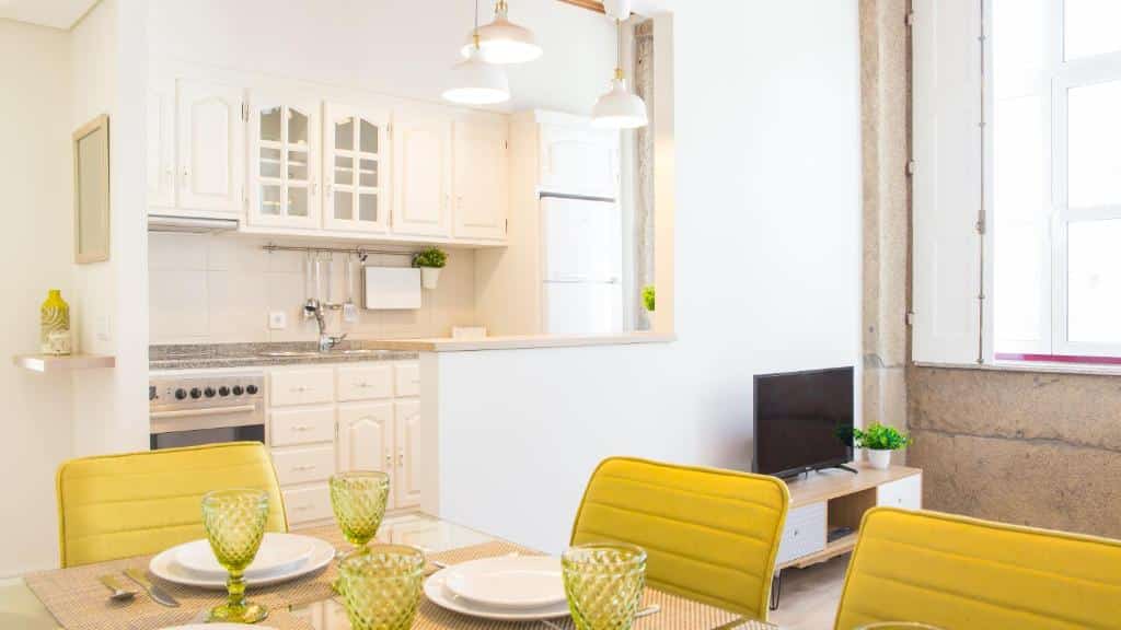 Cozinha e sala de jantar luminosas no Praça 44 – Boutique Apartments, com cadeiras amarelas, copos verdes e uma janela ampla.