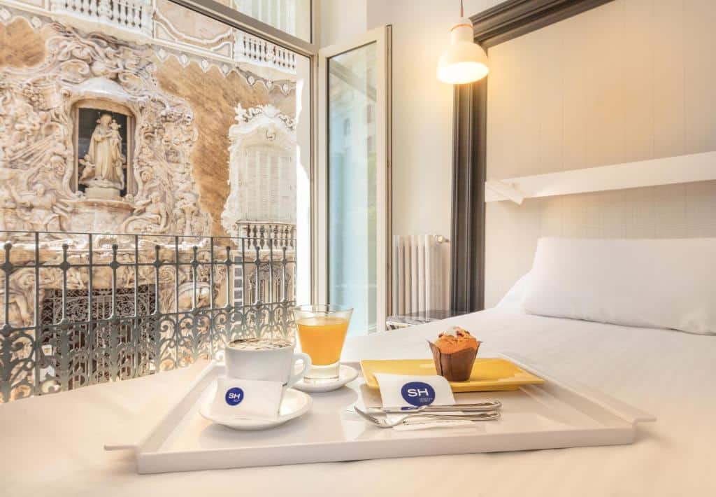 Quarto do SH Ingles Boutique Hotel de decoração em estilo antigo, com parede de relevos ornamentais e uma pintura de figura religiosa, e uma bandeja com bebida e um lanche em primeiro plano.
