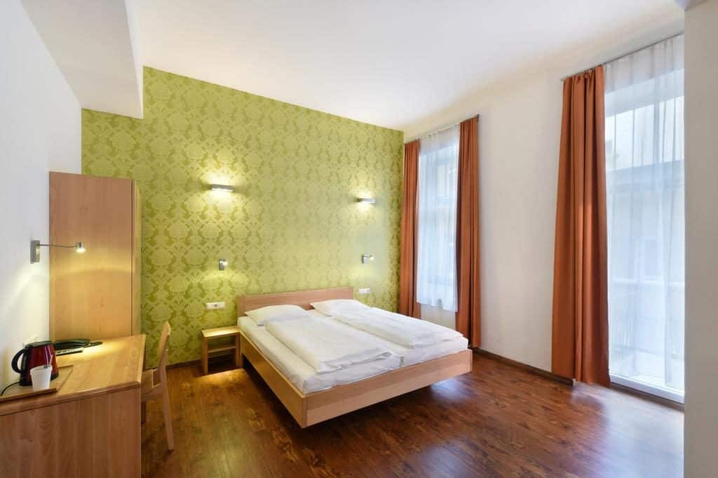 Quarto no Hotel Mocca, com cama de casal, papel de parede verde, janelas altas e cortinados.
