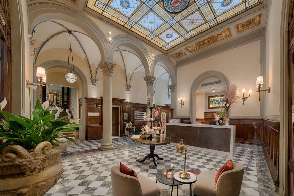 Receção do NH Collection Firenze Porta Rossa, um dos hotéis na Toscana, com decoração clássica, mesa com flores, poltronas com mesa redonda ao centro e escada de acesso aos restantes espaços do hotel